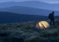 Wild camper pitching a tent on a remote UK hillside at dusk