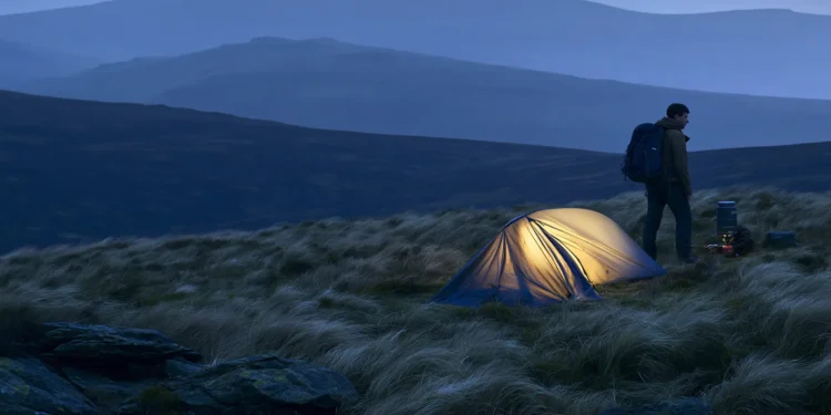 Wild camper pitching a tent on a remote UK hillside at dusk