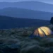 Wild camper pitching a tent on a remote UK hillside at dusk